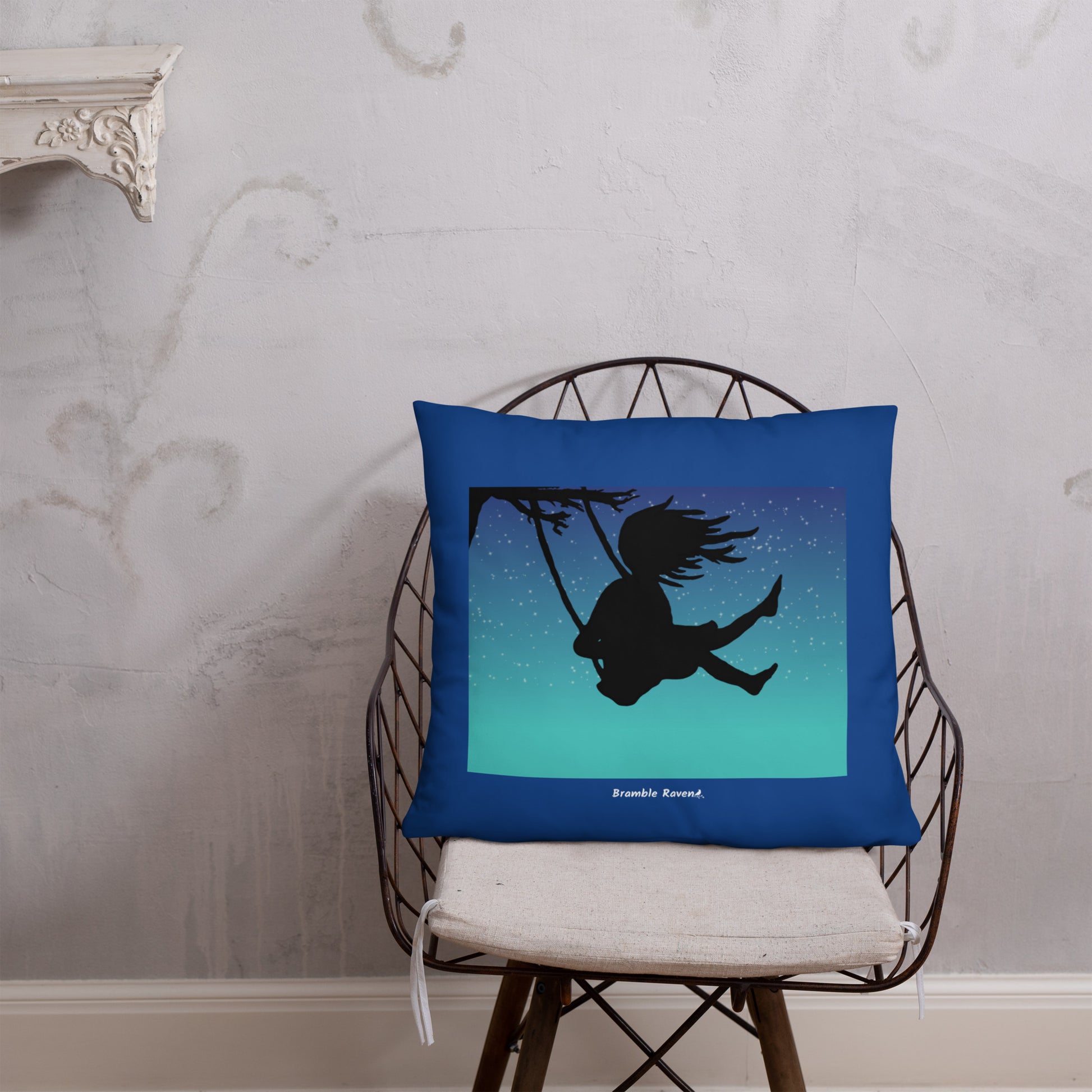 Original Swing Free design of a girl's silhouette in a tree swing against the backdrop of a blue starry sky. Rectangular image on front of pillow with blue background fabric. Pillow has design on both sides. 22 by 22 inch accent pillow. Shown on wicker chair.