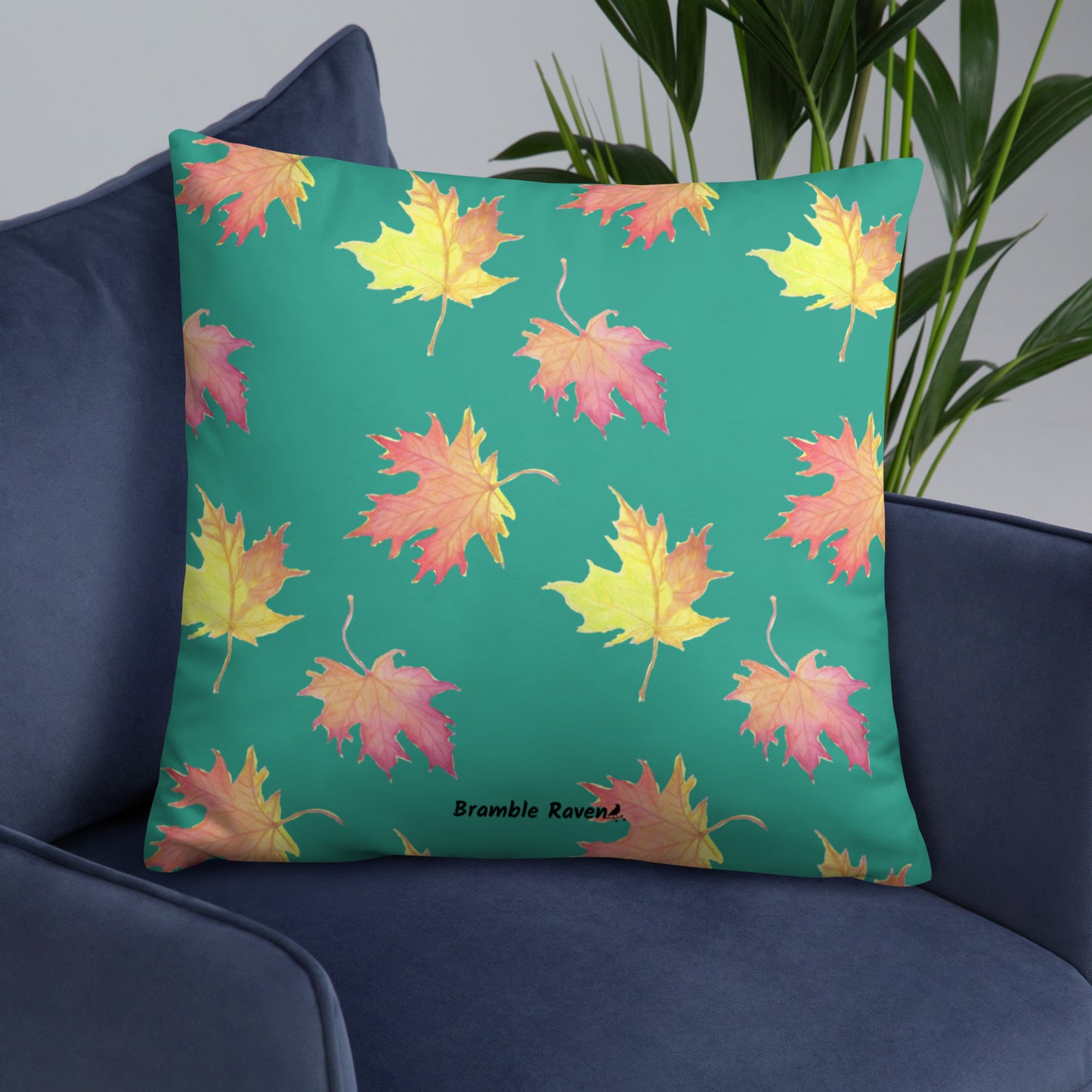 Front of 22 by 22 inch accent pillow featuring watercolor fall leaves on a dark green background. Pillow is double-sided. Larger patterned leaves on the back. Smaller patterned leaves on the front. Shown on a blue sofa.