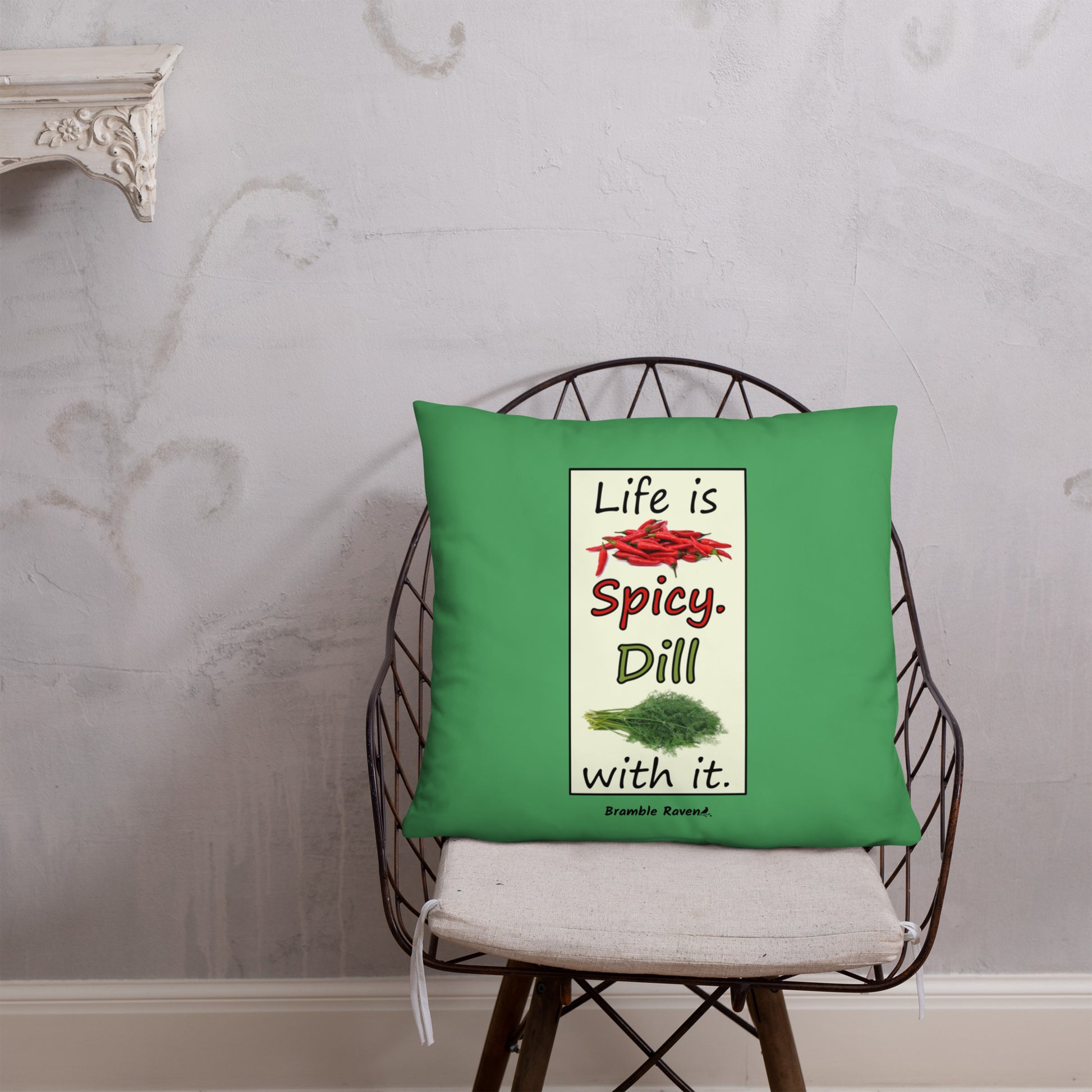 Life is spicy. Dill with it. Phrase with images of chili peppers and dill weed. Rectangular frame for saying on green background. 22 by 22 inch accent pillow. Double sided image. Shown on a wicker chair.
