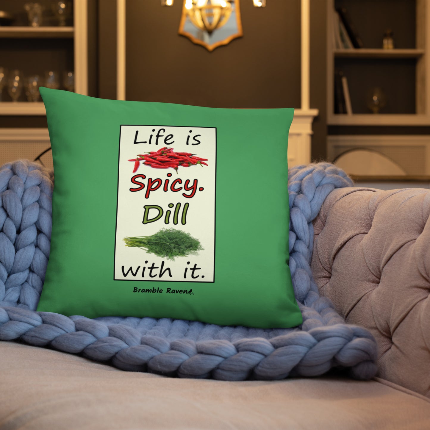 Life is spicy. Dill with it. Phrase with images of chili peppers and dill weed. Rectangular frame for saying on green background. 22 by 22 inch accent pillow. Double sided image. Shown on a blue knitted blanket on a tan couch.