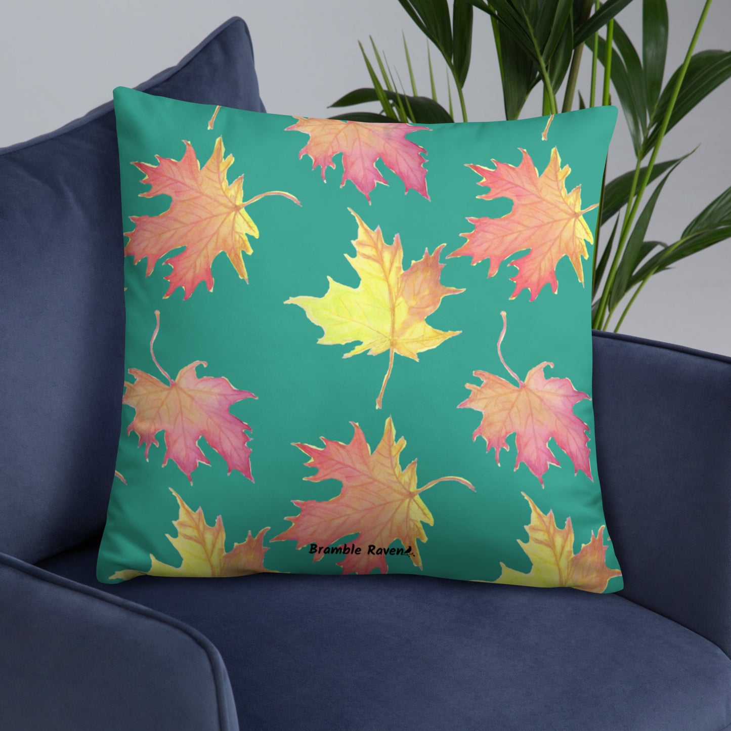 22 by 22 inch accent pillow featuring watercolor fall leaves on a dark green background. Pillow is double-sided. Larger patterned leaves on the back. Smaller patterned leaves on the front. Shown on a blue sofa.