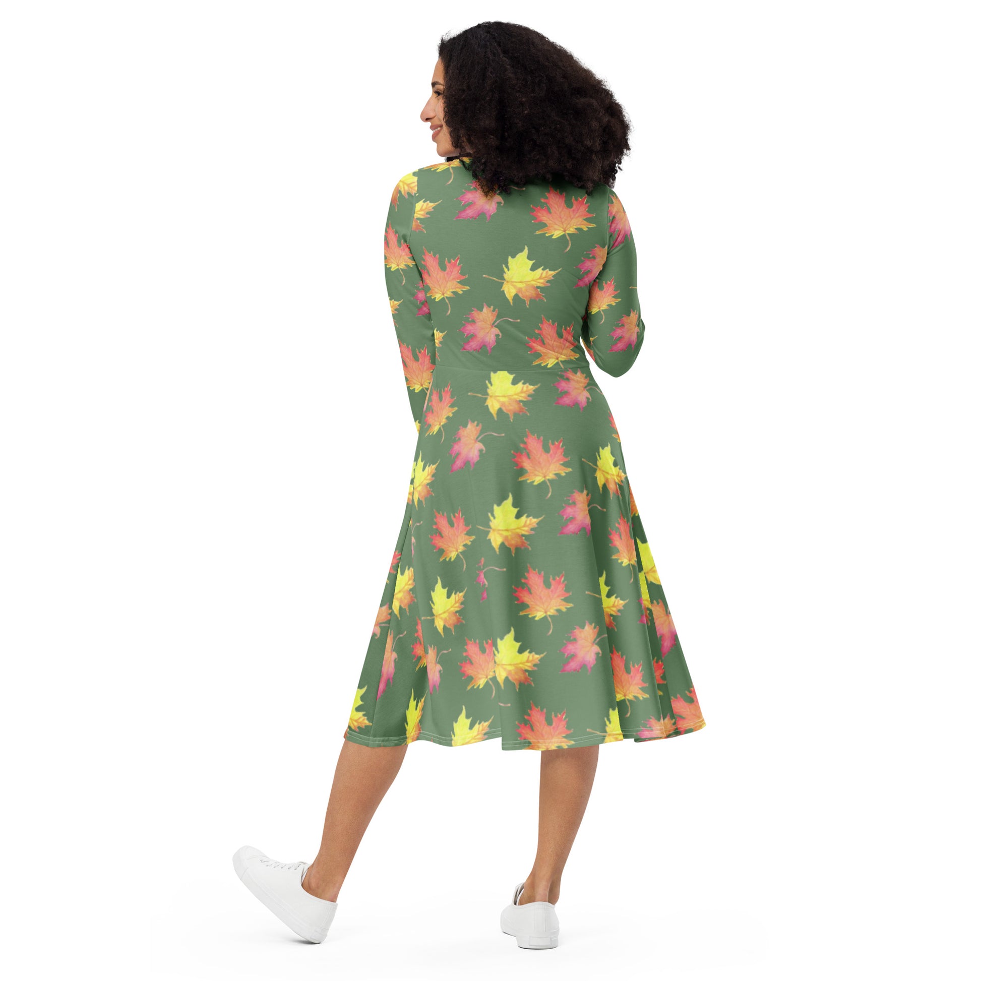 Long sleeve midi dress. Watercolor fall leaves patterned over an amulet green background. Soft and flattering fit. Boatline neck, fitted waist, flared bottom, and side pockets. Photo shows back view of dress on female model.