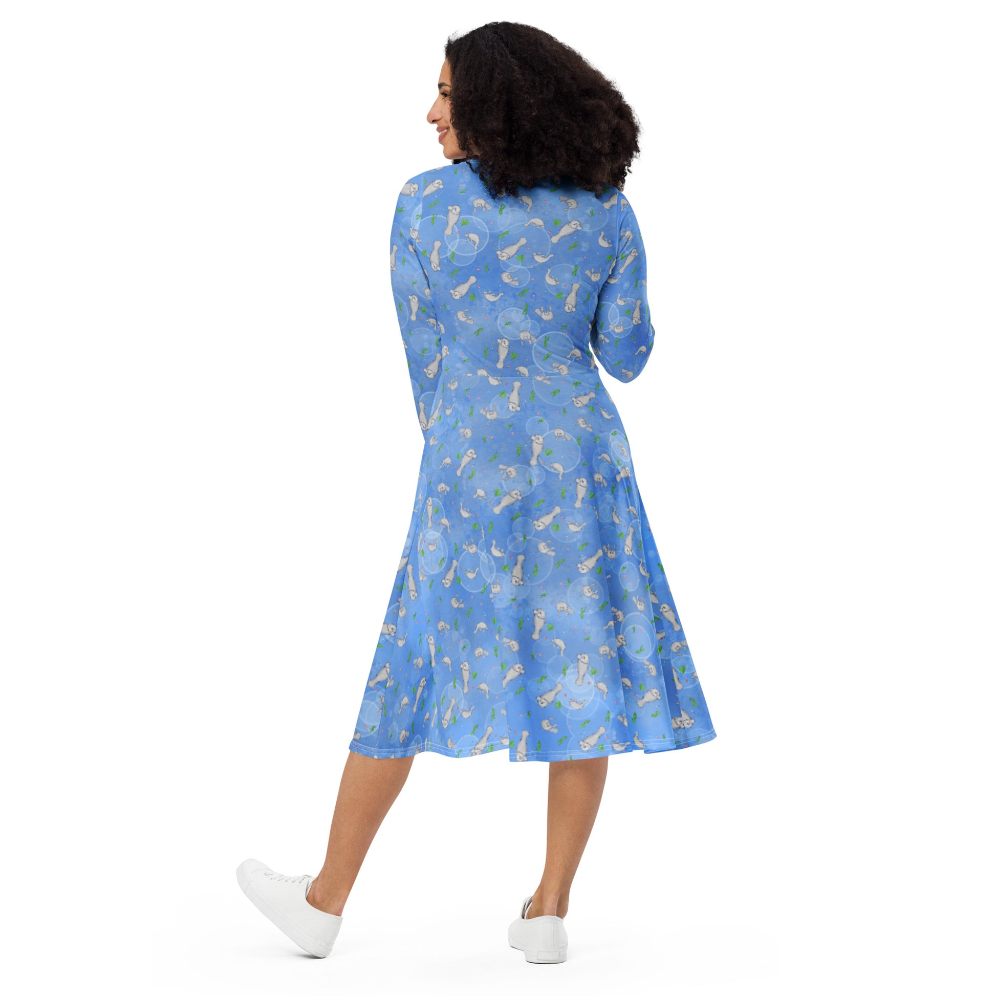 Long sleeve midi dress with fitted waist, flared bottom, and side pockets. Features a patterned design of manatees, seashells, seaweed, and bubbles on an ocean blue background. Back view on female model.