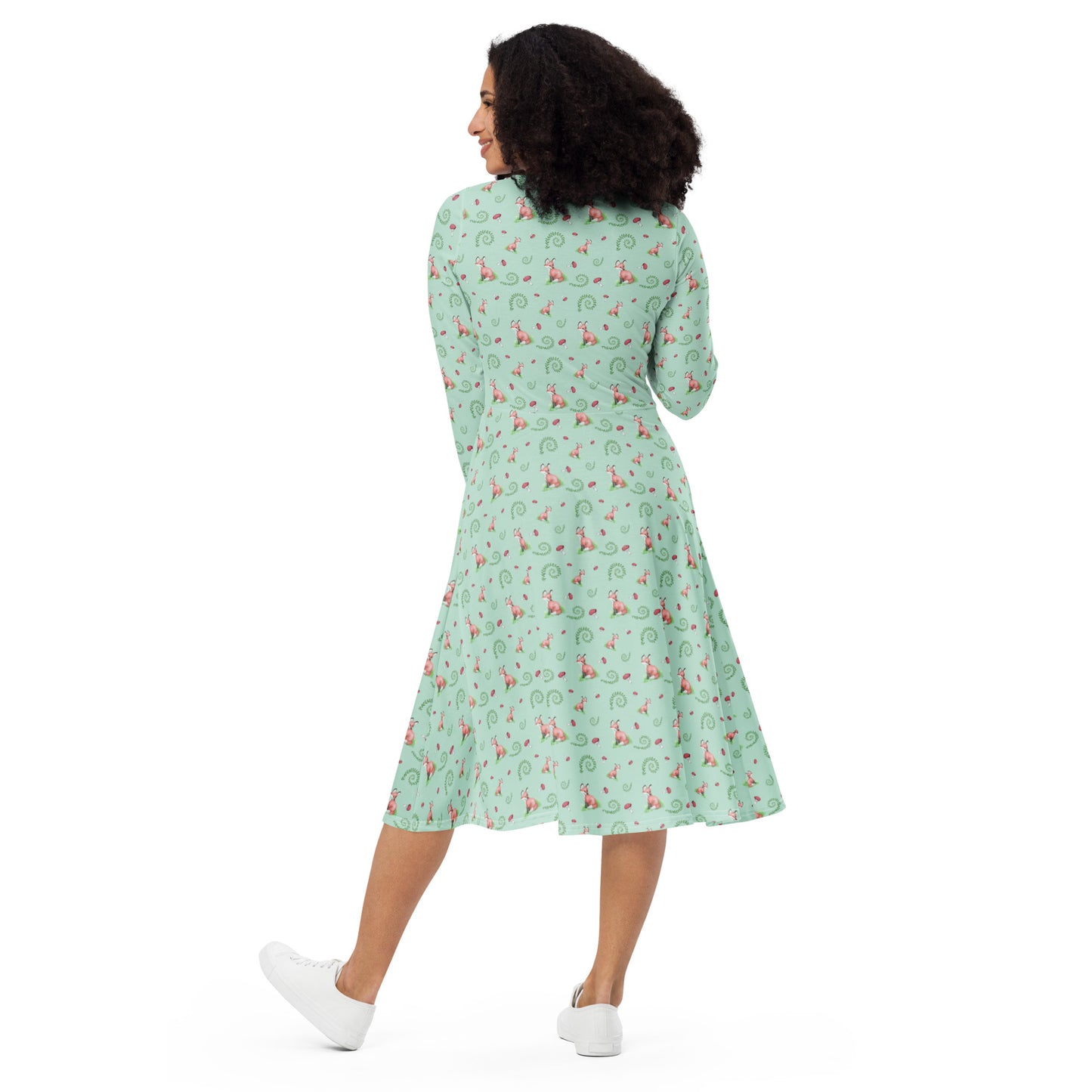 Forest fox patterned long sleeve midi dress with side pockets. Has watercolor foxes, mushrooms, and ferns on a light green fabric. Features boat neckline and fitted elastic waist. Back view on female model.