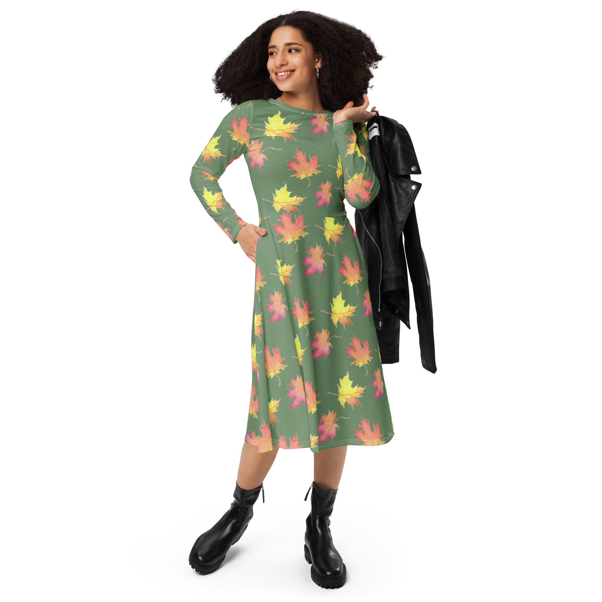 Long sleeve midi dress. Watercolor fall leaves patterned over an amulet green background. Soft and flattering fit. Boatline neck, fitted waist, flared bottom, and side pockets. Photo shows dress on female model holding jacket over shoulder.