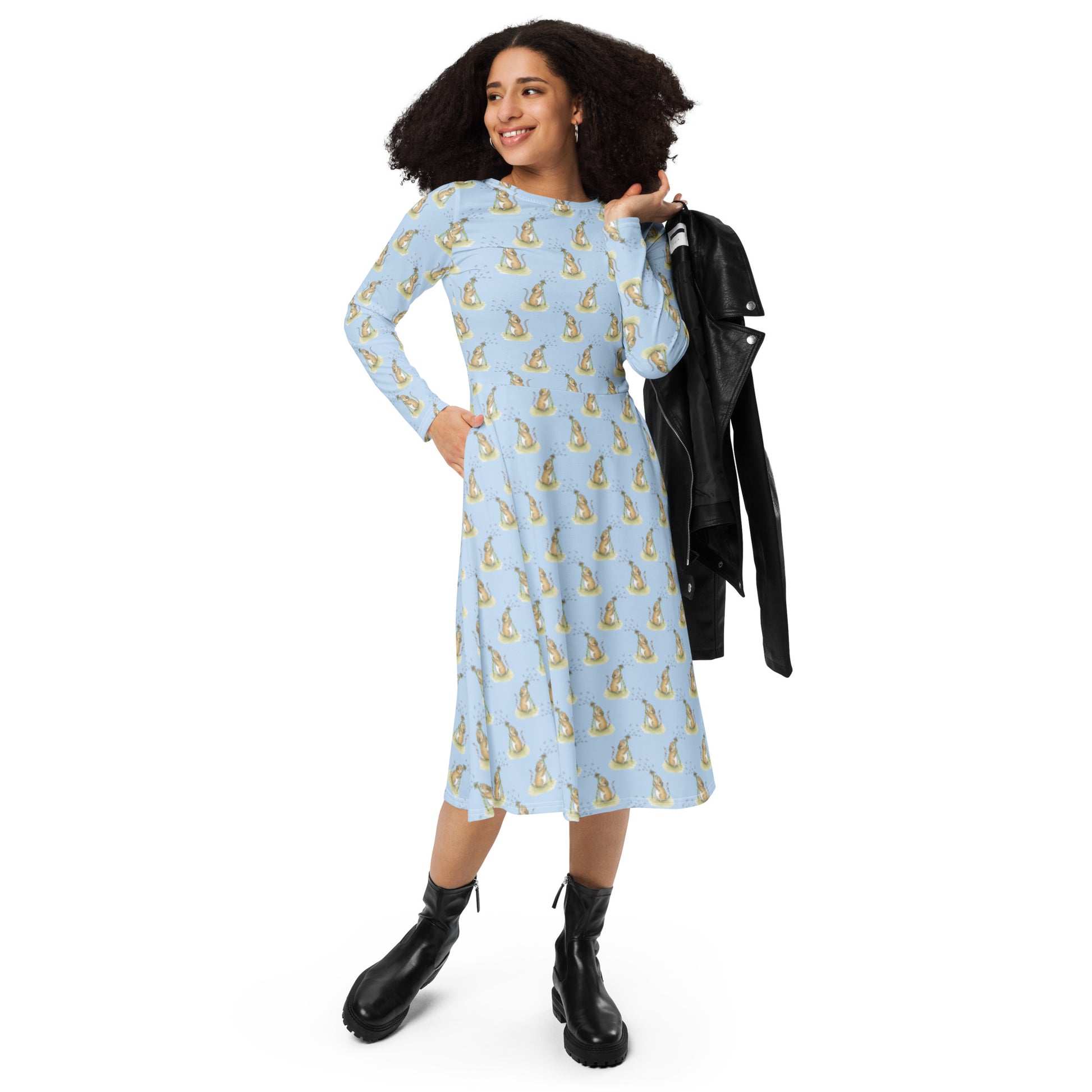 Dandelion Wish patterned long sleeve midi dress. Features patterned design of a mouse making a wish on a dandelion fluff against a light blue background. Dress has boat neckline, fitted waist, flared bottom, and side pockets.  Shown on female model with black jacket over her shoulder.