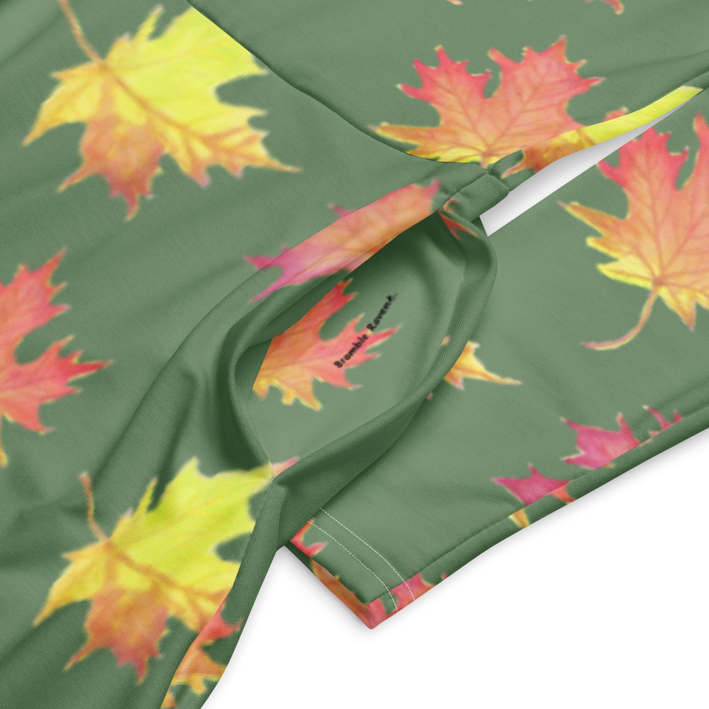 Long sleeve midi dress. Watercolor fall leaves patterned over an amulet green background. Soft and flattering fit. Boatline neck, fitted waist, flared bottom, and side pockets. Closeup detail of pocket and sleeve.