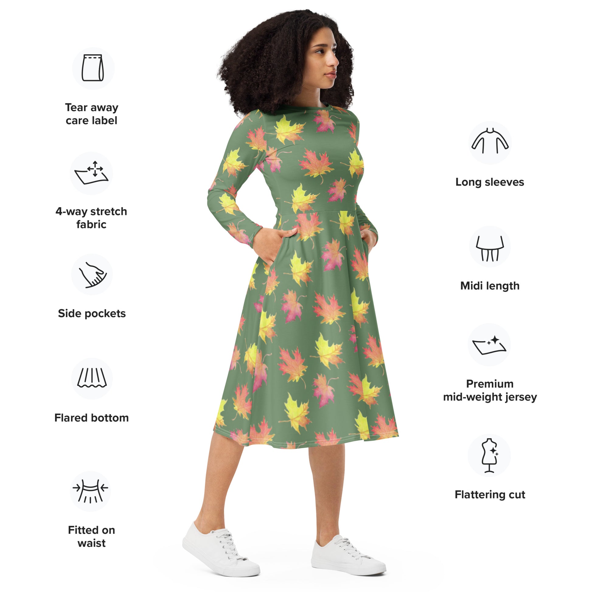 Long sleeve midi dress. Watercolor fall leaves patterned over an amulet green background. Soft and flattering fit. Boatline neck, fitted waist, flared bottom, and side pockets. Shown on female model with hands in her pockets.