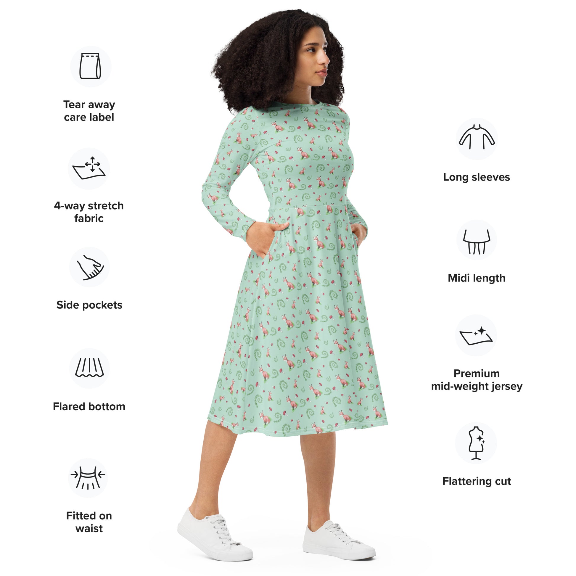 Forest fox patterned long sleeve midi dress with side pockets. Has watercolor foxes, mushrooms, and ferns on a light green fabric. Features boat neckline and fitted elastic waist. Shown on female model.