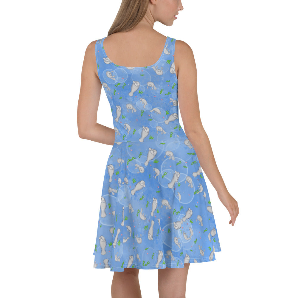 Sleeveless skater dress that features manatees on on ocean blue background. The soft fabric is made of 82% polyester and 18% spandex, so it is both smooth and stretchy. It has a mid-thigh length flared skirt and elastic waistline. Back view on female model.