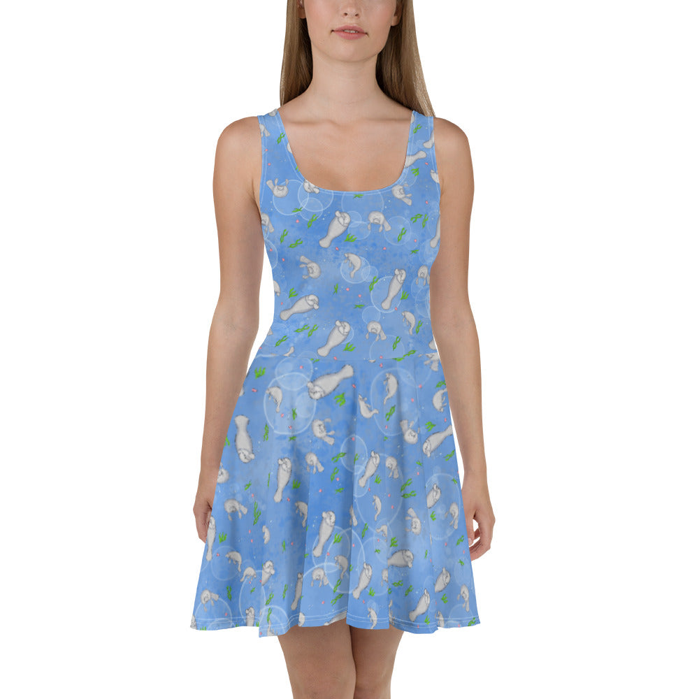 Sleeveless skater dress that features manatees on on ocean blue background. The soft fabric is made of 82% polyester and 18% spandex, so it is both smooth and stretchy. It has a mid-thigh length flared skirt and elastic waistline. Shown on female model.