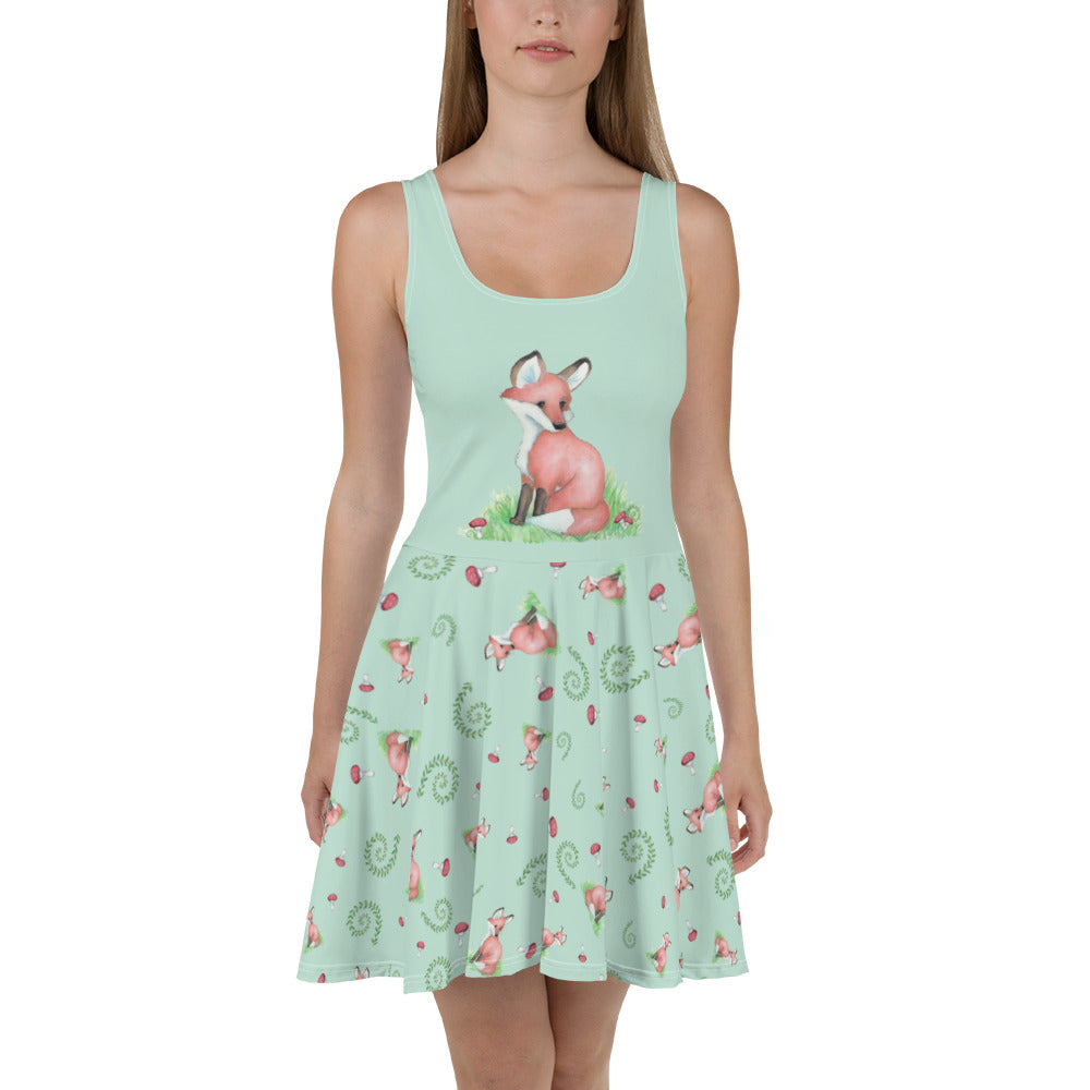 Sleeveless skater dress featuring watercolor foxes, mushrooms, and ferns on a light green fabric. Mid-thigh length flared skirt with a fitted elastic waist. Shown on female model.