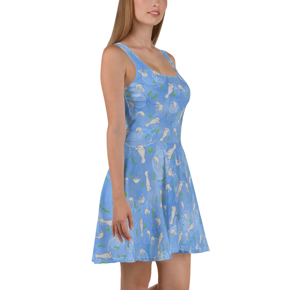 Sleeveless skater dress that features manatees on on ocean blue background. The soft fabric is made of 82% polyester and 18% spandex, so it is both smooth and stretchy. It has a mid-thigh length flared skirt and elastic waistline. Shown on female model facing right.