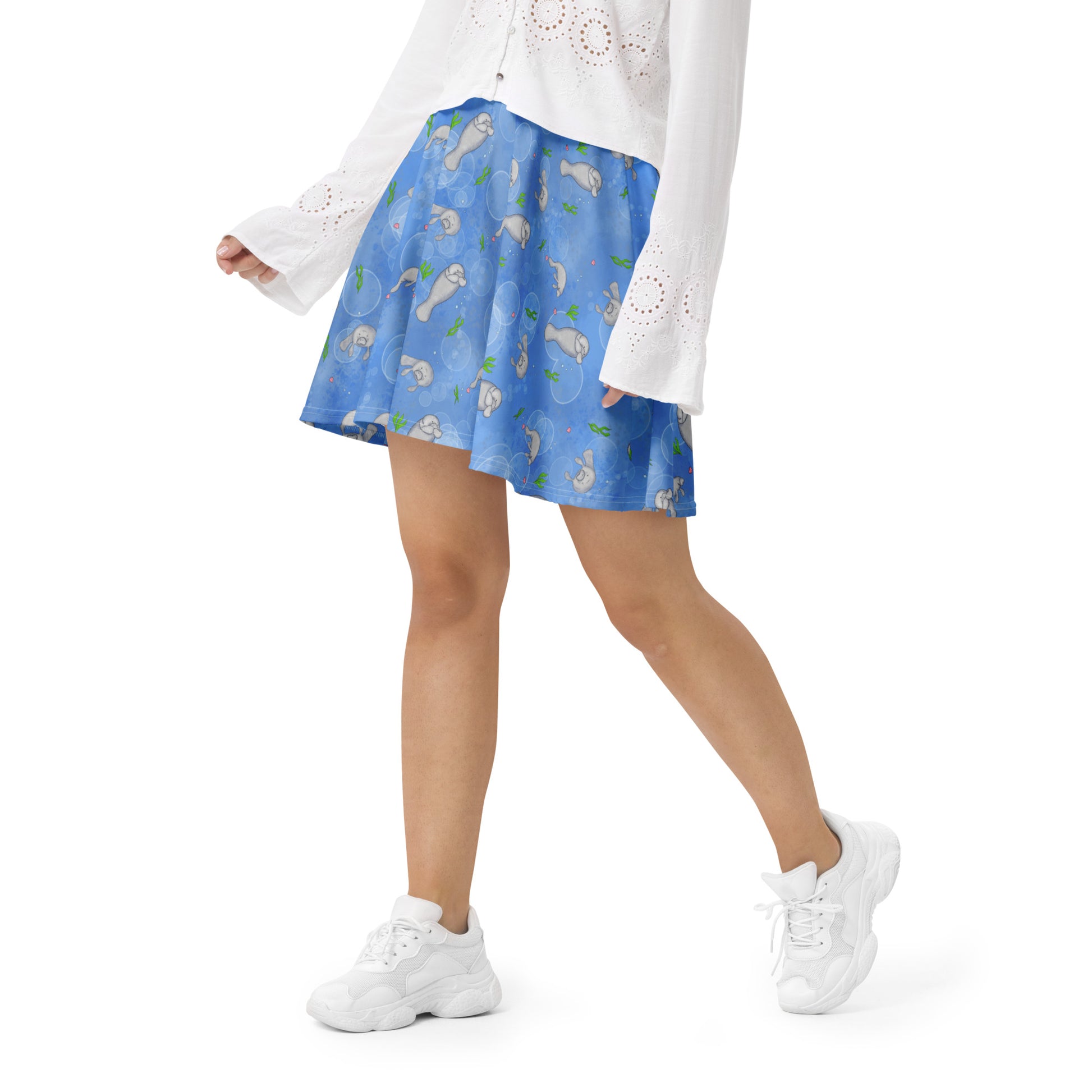 Manatee patterned skater skirt with elastic waist and mid-thigh length skirt. Has a pattern of manatees, seashells, seaweed and bubbles on a blue background. Shown on female model with white sweater and shoes.