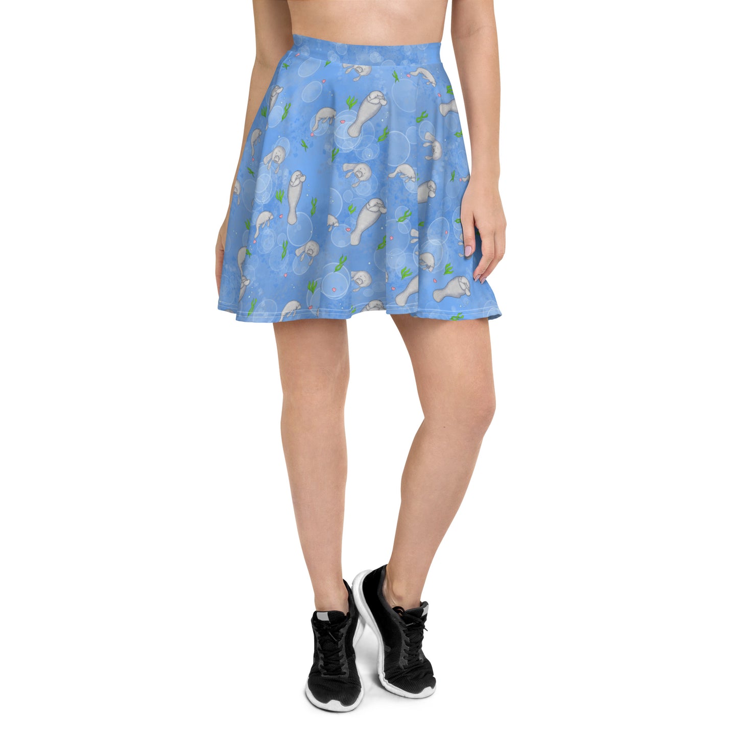 Manatee patterned skater skirt with elastic waist and mid-thigh length skirt. Has a pattern of manatees, seashells, seaweed and bubbles on a blue background. Shown on female model with black shoes.