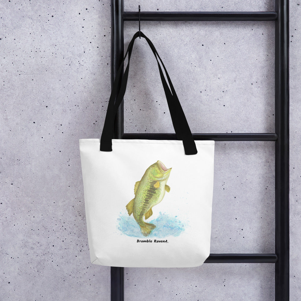White polyester 15 by 15 inch tote bag. Features a watercolor painting of a largemouth bass leaping out of the water. Black handles. Shown hanging from a black ladder.