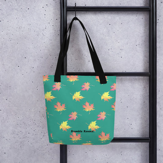 15 by 15 inch polyester tote bag featuring watercolor fall leaves on a dark green background. Bag has black handles. Shown hanging on a black ladder.