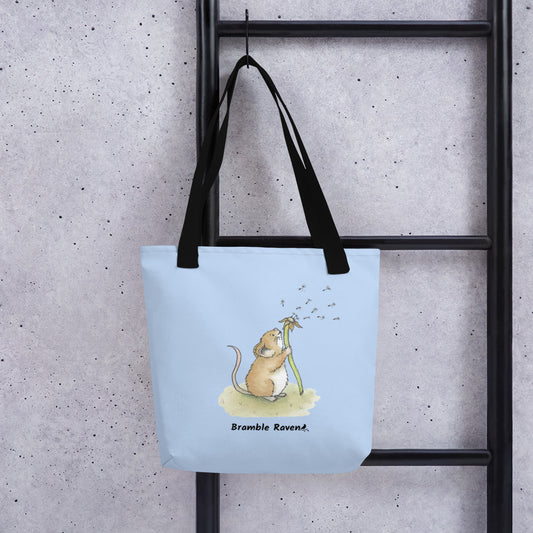 Original Dandelion Wish design of cute watercolor mouse blowing dandelion seeds. on light blue background. Double sided image on polyester tote bag with black handles. 15 by 15 inches in size. Shown hanging on ladder.