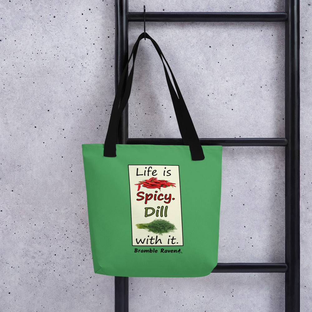 Life is spicy. Dill with it. Phrase with images of chili peppers and dill weed. Rectangular frame for saying on a green background. Polyester tote bag with black handles. 15 by 15 inches. Double sided image. Shown hanging on a black ladder.
