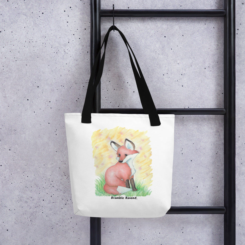 15 by 15 inch white polyester tote bag with black handles. Features original watercolor painting of a fox in the grass against a yellow background. Shown hanging on a black ladder.