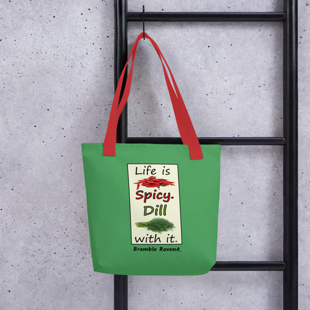 Life is spicy. Dill with it. Phrase with images of chili peppers and dill weed. Rectangular frame for saying on a green background. Polyester tote bag with red handles. 15 by 15 inches. Double sided image. Shown hanging on a black ladder.