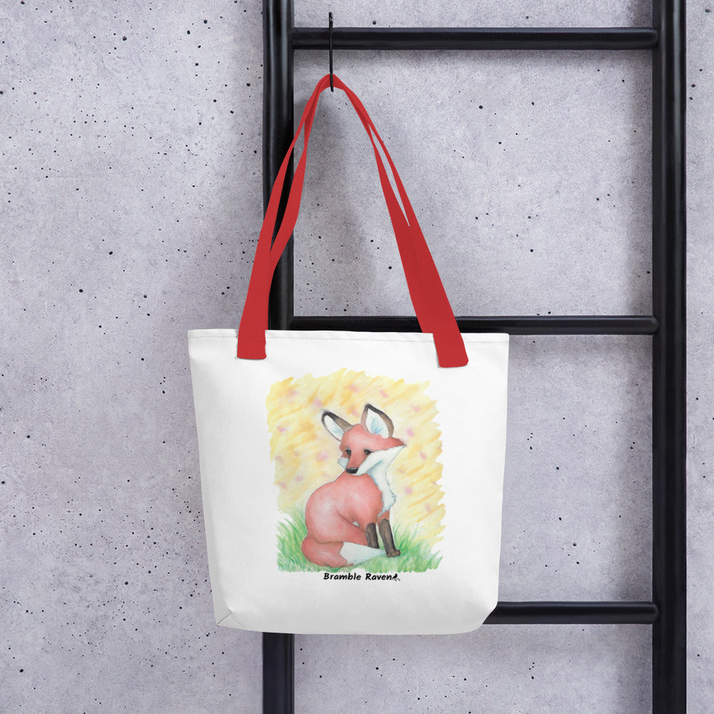 15 by 15 inch white polyester tote bag with red handles. Features original watercolor painting of a fox in the grass against a yellow background. Shown hanging on a black ladder.