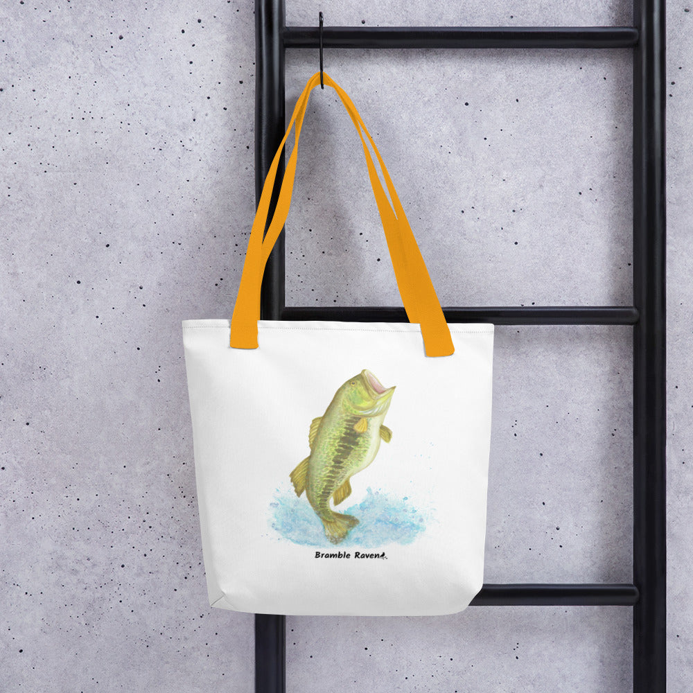 White polyester 15 by 15 inch tote bag. Features a watercolor painting of a largemouth bass leaping out of the water. Yellow handles. Shown hanging from a black ladder.