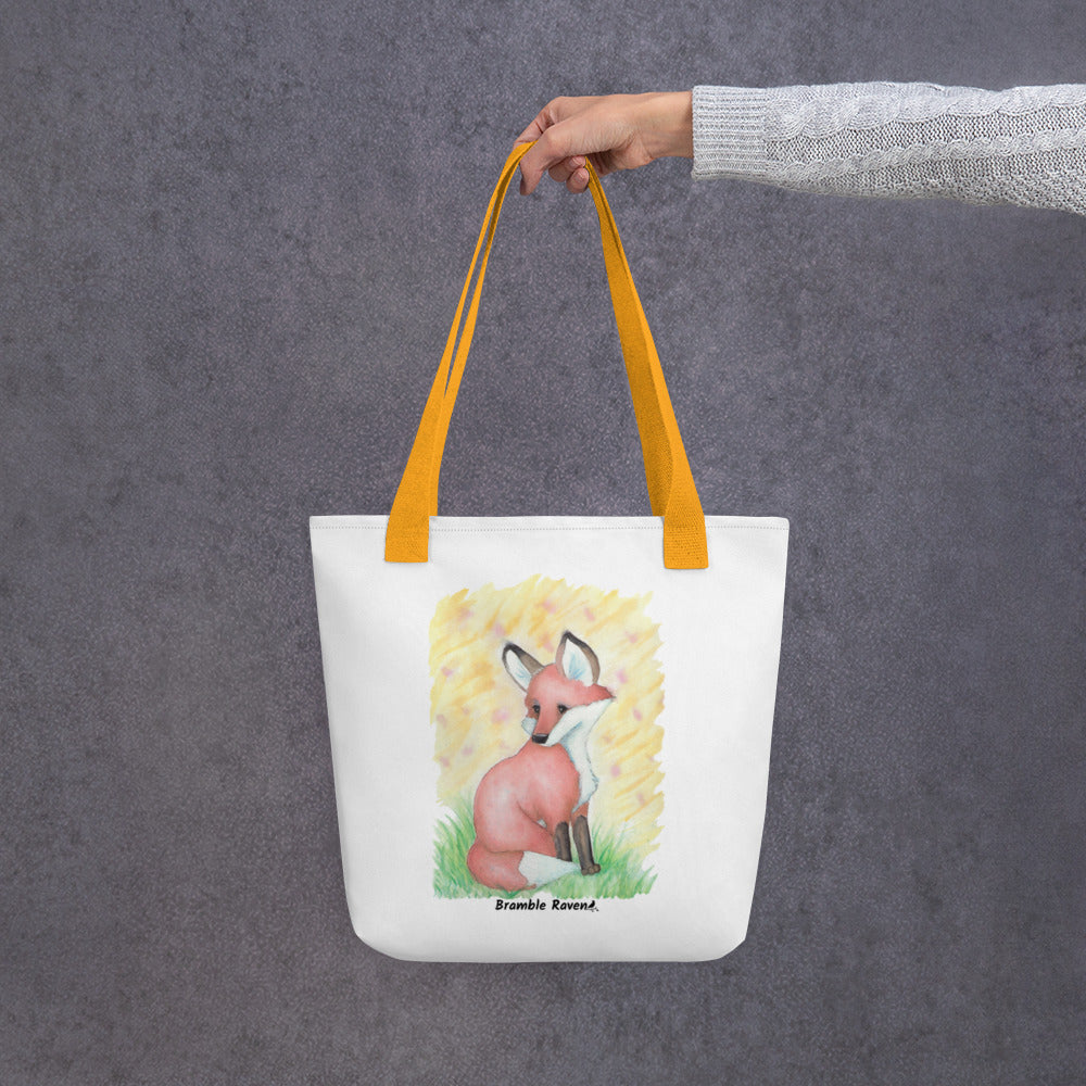 15 by 15 inch white polyester tote bag with yellow handles. Features original watercolor painting of a fox in the grass against a yellow background. Shown hanging from a model's hand.