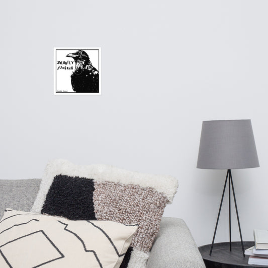 10 by 10 inch matte poster with silently judging text by black crow wearing a monocle in a square on a white background. Shown on wall above sofa and lamp.
