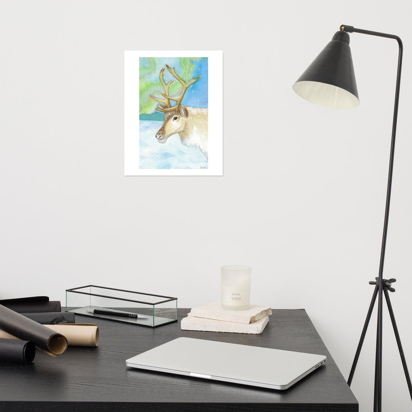 11 by 14 inch art poster print. Watercolor painting of a snowy reindeer with the northern lights in the background. Shown on the wall above a grey desk and lamp.