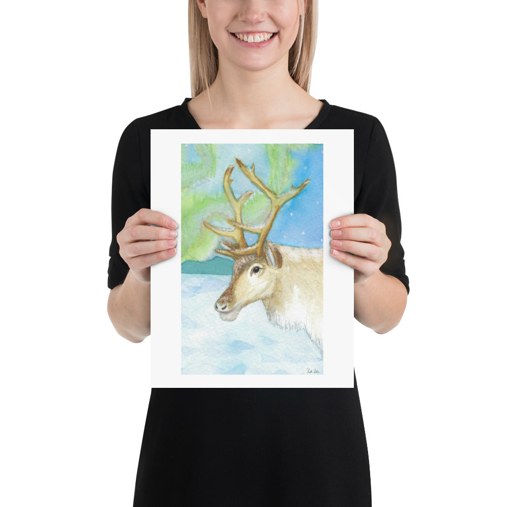 11 by 14 inch art poster print. Watercolor painting of a snowy reindeer with the northern lights in the background. Shown being held by female model.