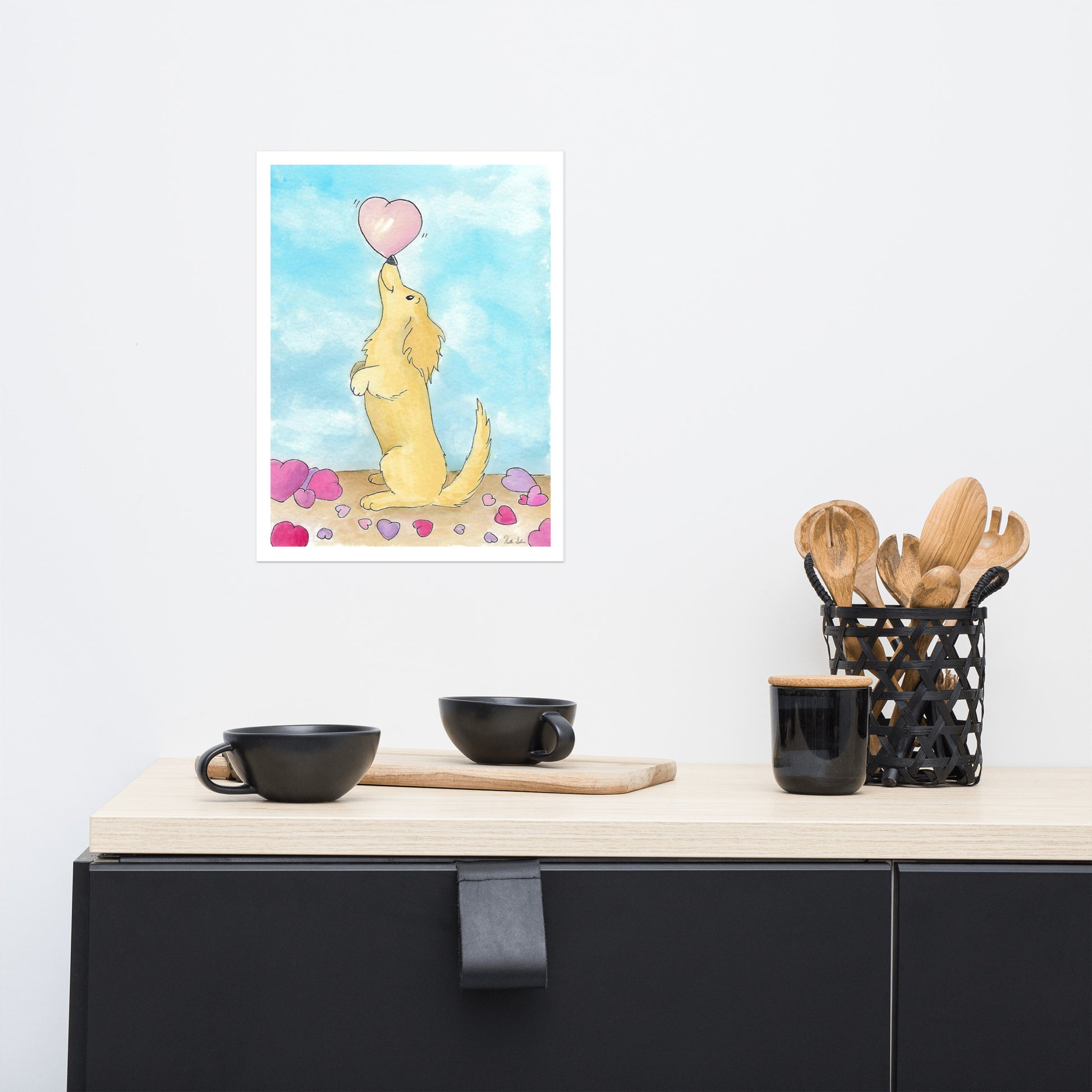 12 x 16 inch enhanced matte paper art print. Watercolor painting entitled Puppy love. Design shows a cute puppy balancing a heart on its nose, with hearts on the floor and a blue sky background. Shown on wall above kitchen counter with bowls and utensils.