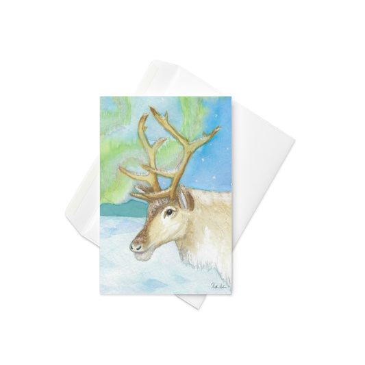 4 x 6 inch greeting card. Features watercolor print of a reindeer in the snow with northern lights in the sky. Blank inside. Comes with a white envelope.