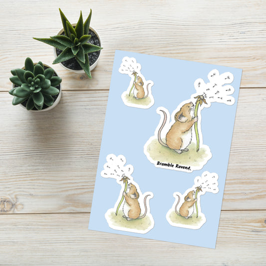 Original Dandelion Wish design of cute watercolor mouse blowing dandelion seeds. Glossy sticker sheet with four mice in different sizes and directions. Each sticker is kiss cut with a white border.  Shown on table with potted plants.