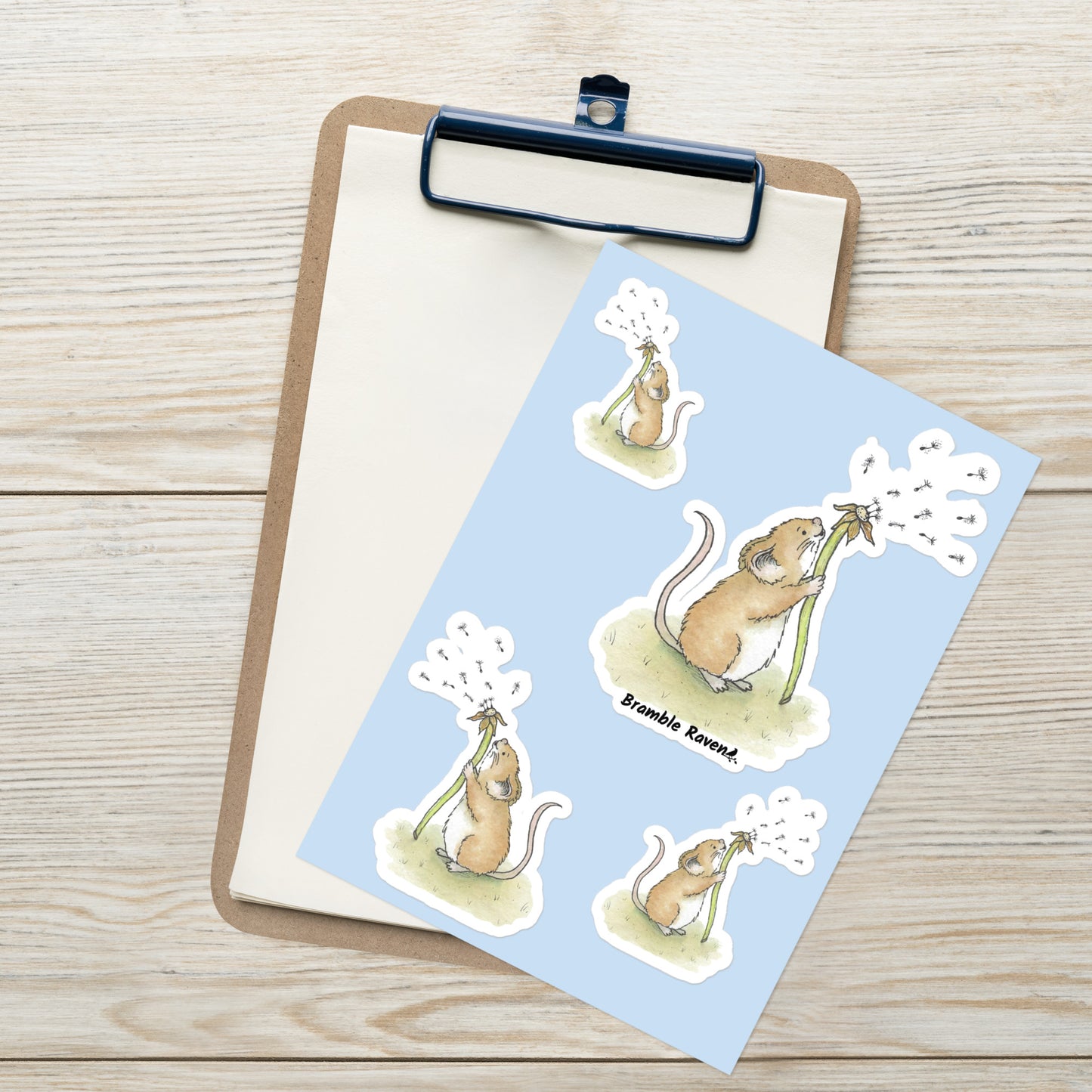 Original Dandelion Wish design of cute watercolor mouse blowing dandelion seeds. Glossy sticker sheet with four mice in different sizes and directions. Each sticker is kiss cut with a white border.  Shown on clipboard.