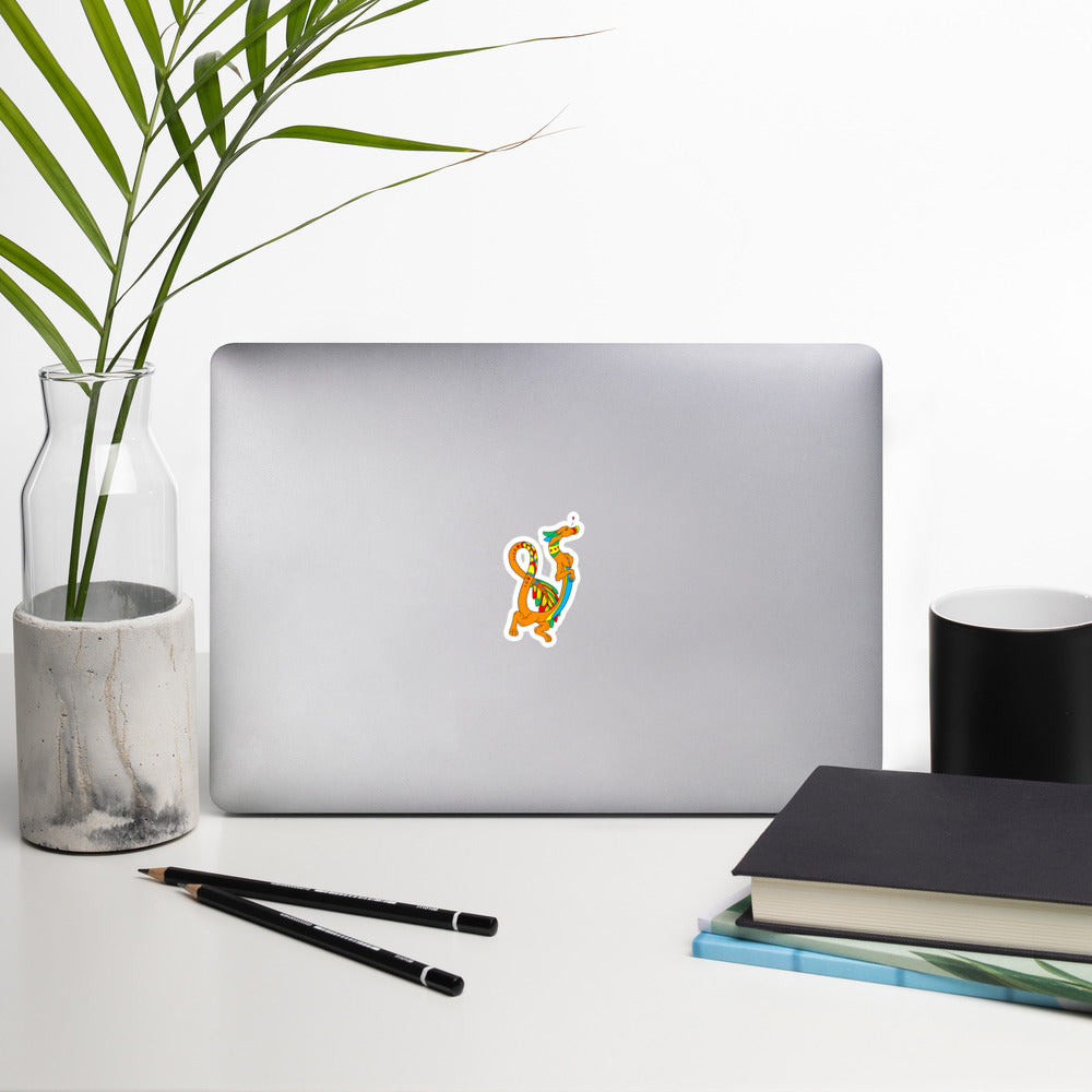 Domingo the Aztec Fuzzy Noodle Dragon. Original character design kiss-cut vinyl sticker with white border. 3 inches tall. Shown on a laptop.