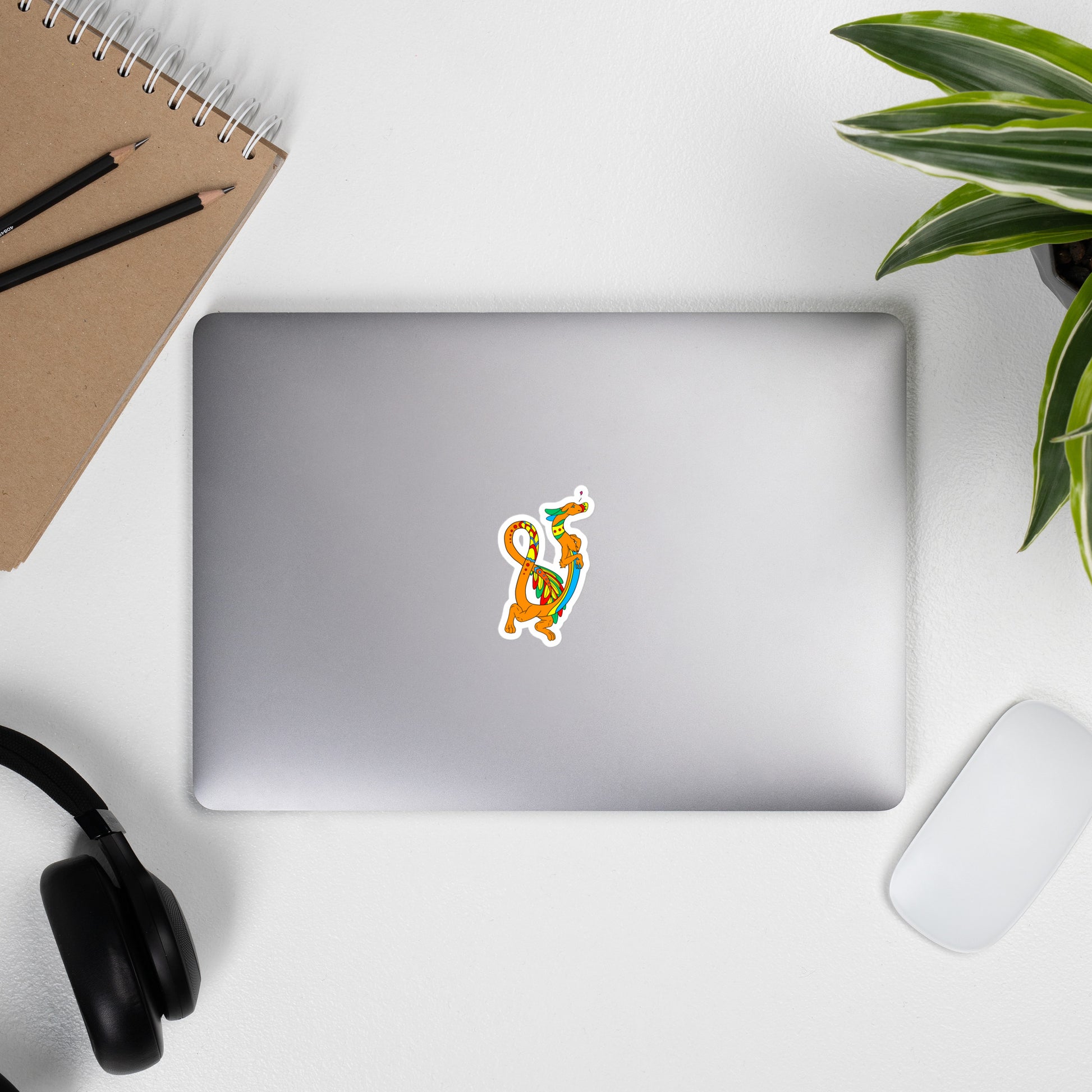 Domingo the Aztec Fuzzy Noodle Dragon. Original character design kiss-cut vinyl sticker with white border. 3 inches tall. Shown on a laptop.