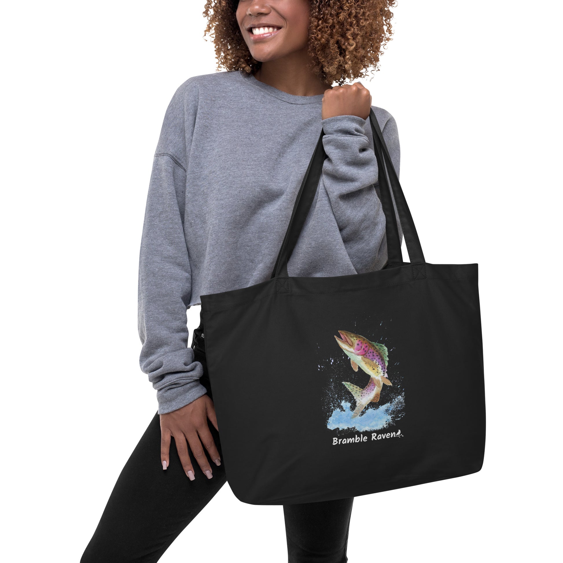 Original watercolor rainbow trout painting with water splashes. Printed on large black colored eco tote. 20 by 14 by 5 inches. 100% recycled cotton. Shown being held by female model.