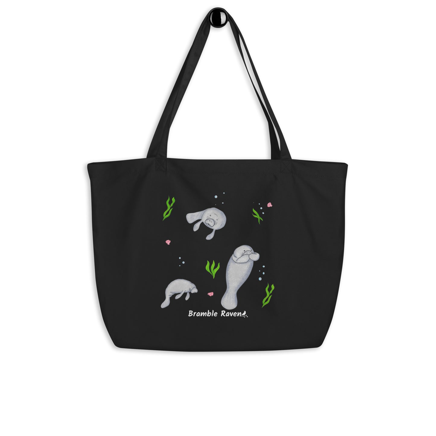 20″ × 14″ × 5″ 100% organic cotton tote bag. Features three manatees with accents of seashells, seaweed, and bubbles. Black fabric with dual handles. Shown hanging on a knob.