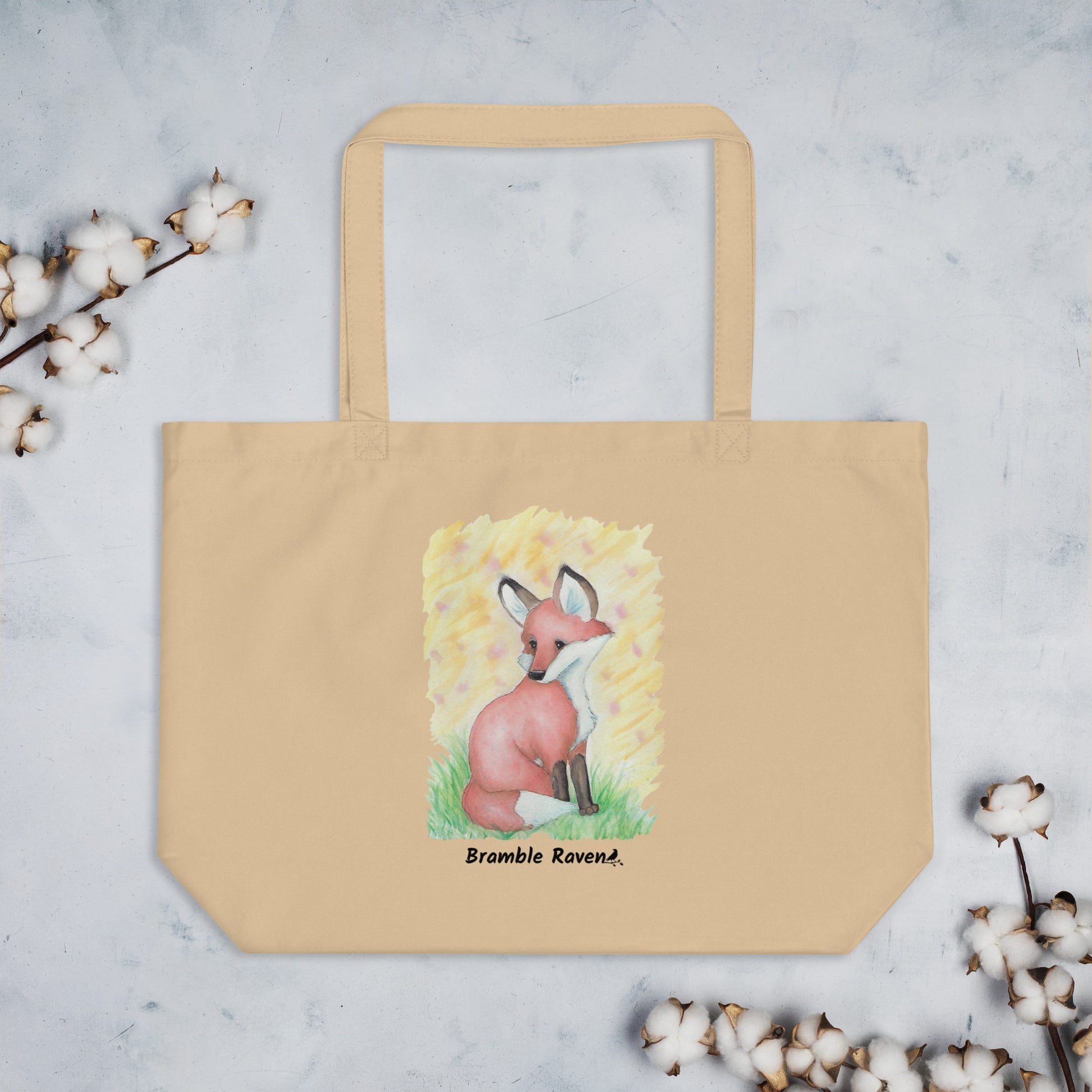 Original watercolor fox painting in the grass with yellow background. Printed on large oyster-colored eco tote. 20 by 14 by 5 inches. 100% recycled cotton. Shown on tabletop with cotton plant accents.