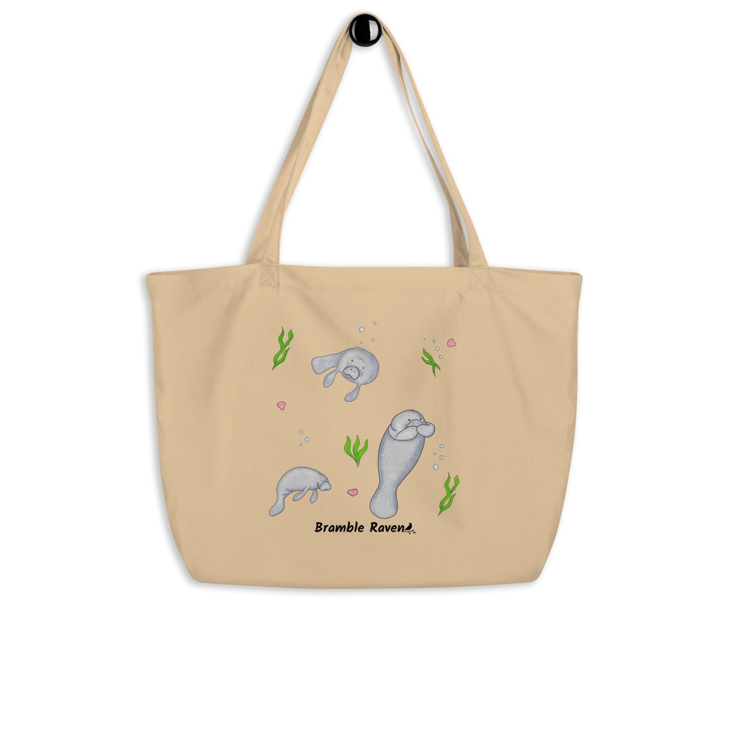 20″ × 14″ × 5″ 100% organic cotton tote bag. Features three manatees with accents of seashells, seaweed, and bubbles. Oyster colored fabric with dual handles. Shown hanging on a knob.