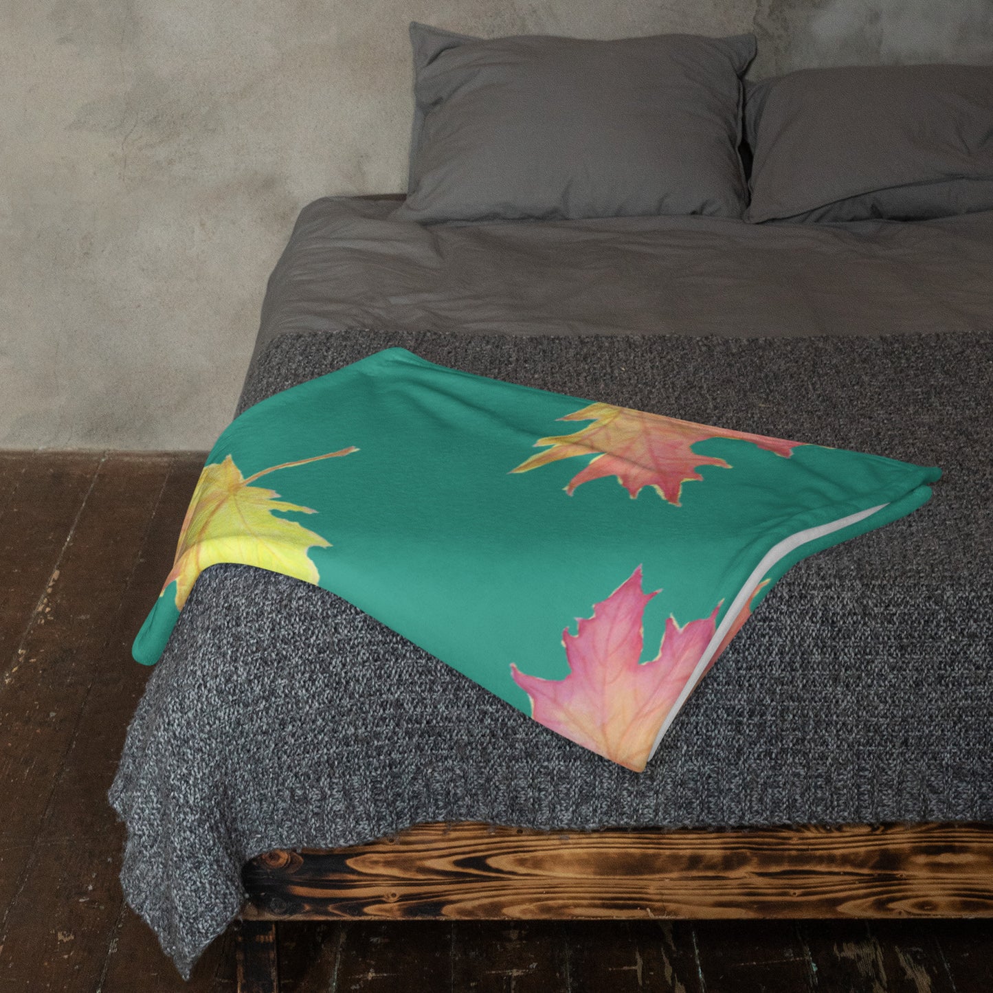 50 by 60 inch soft throw blanket featuring watercolor fall leaves patterned on a dark green background. Shown folded at the foot of a bed.