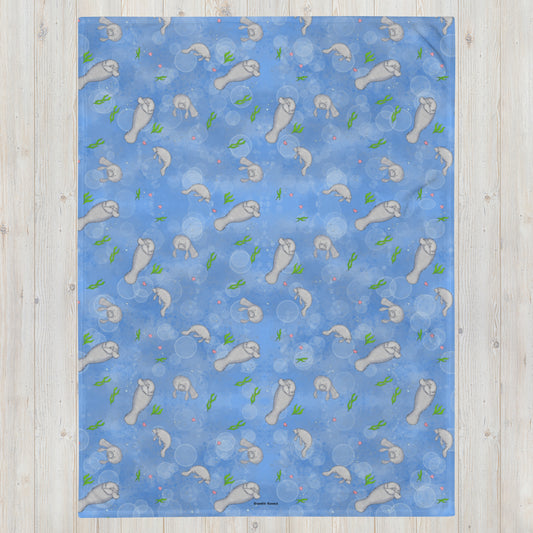 60 x 80 inch polyester throw blanket. Features a patterned print of manatees, seaweed, seashells, and bubbles on a blue background. Printed on front with white underside. Soft silk touch feel. Flame retardant, hypoallergenic, and machine washable.