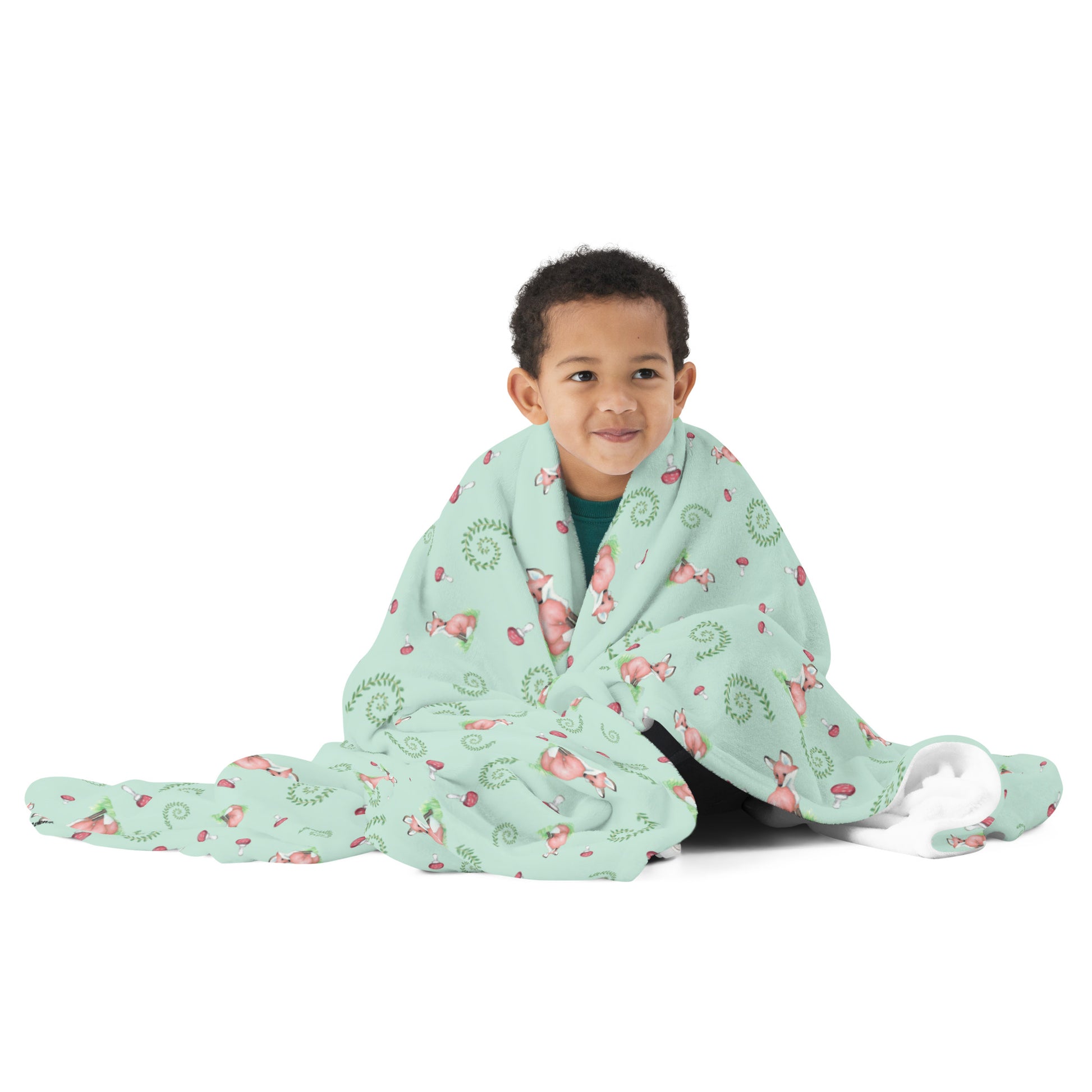 60 by 80 inch watercolor forest fox patterned blanket. Made of soft and fluffy polyester. Has foxes, mushrooms, and ferns on light green background. White underside. Machine-washable, hypoallergenic, and flame retardant. Shown wrapped around a child.