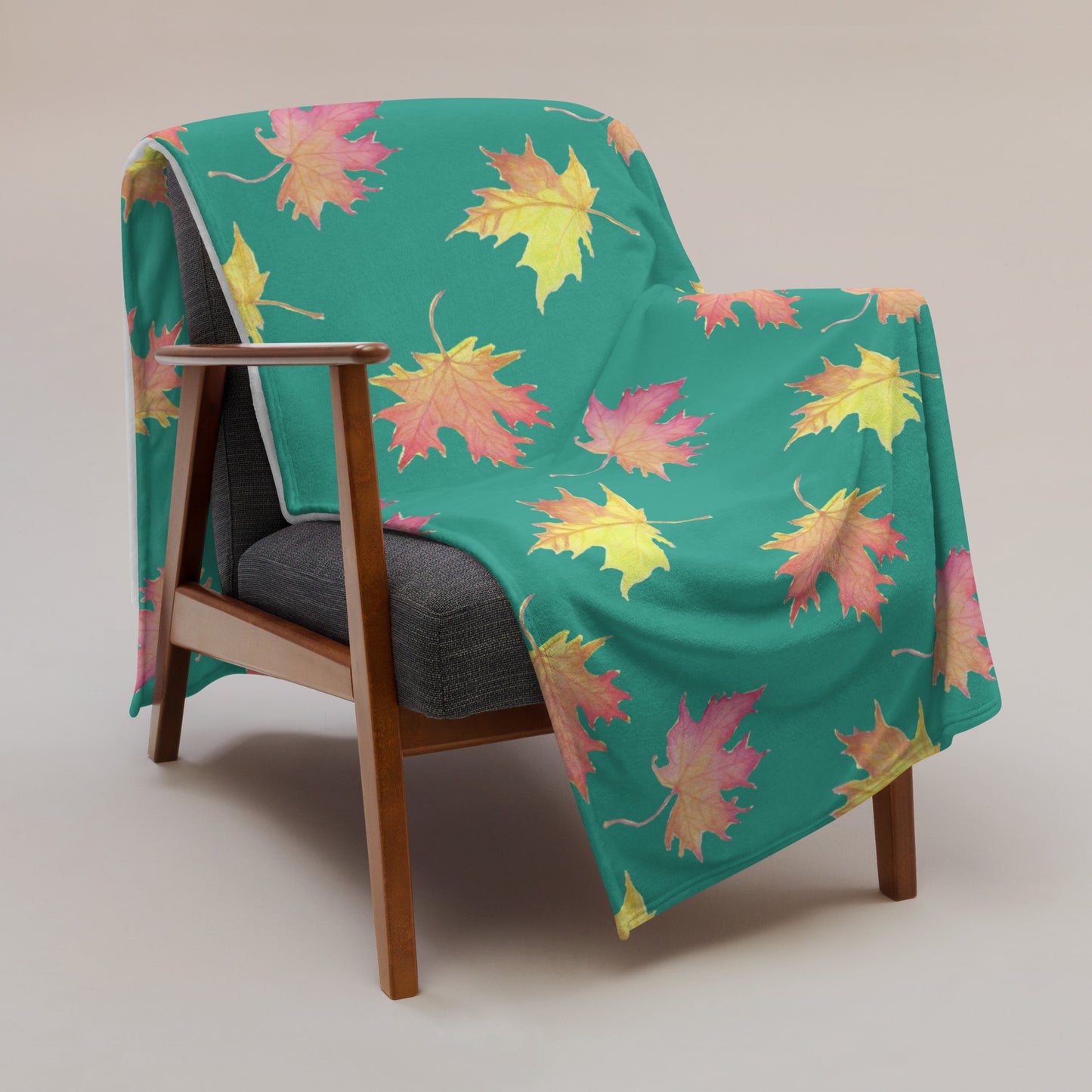 60 by 80 inch soft throw blanket featuring watercolor fall leaves patterned on a dark green background. Shown draped across a chair.