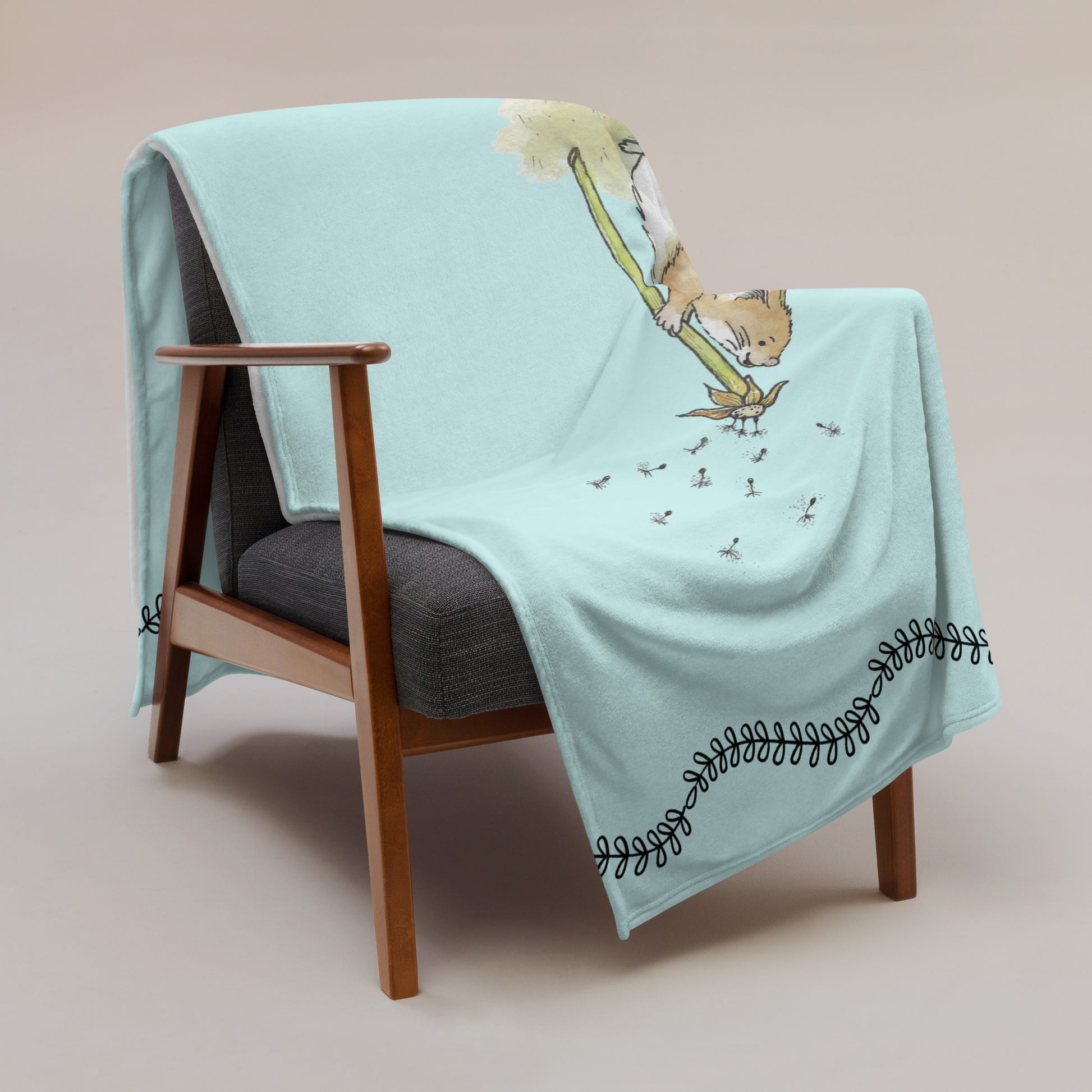Original Dandelion Wish design of cute watercolor mouse blowing dandelion seeds on a light blue background. Black vine border on top and bottom. Make a Wish phrase below mouse graphic. 50 by 60 inch throw blanket. draped over chair.
