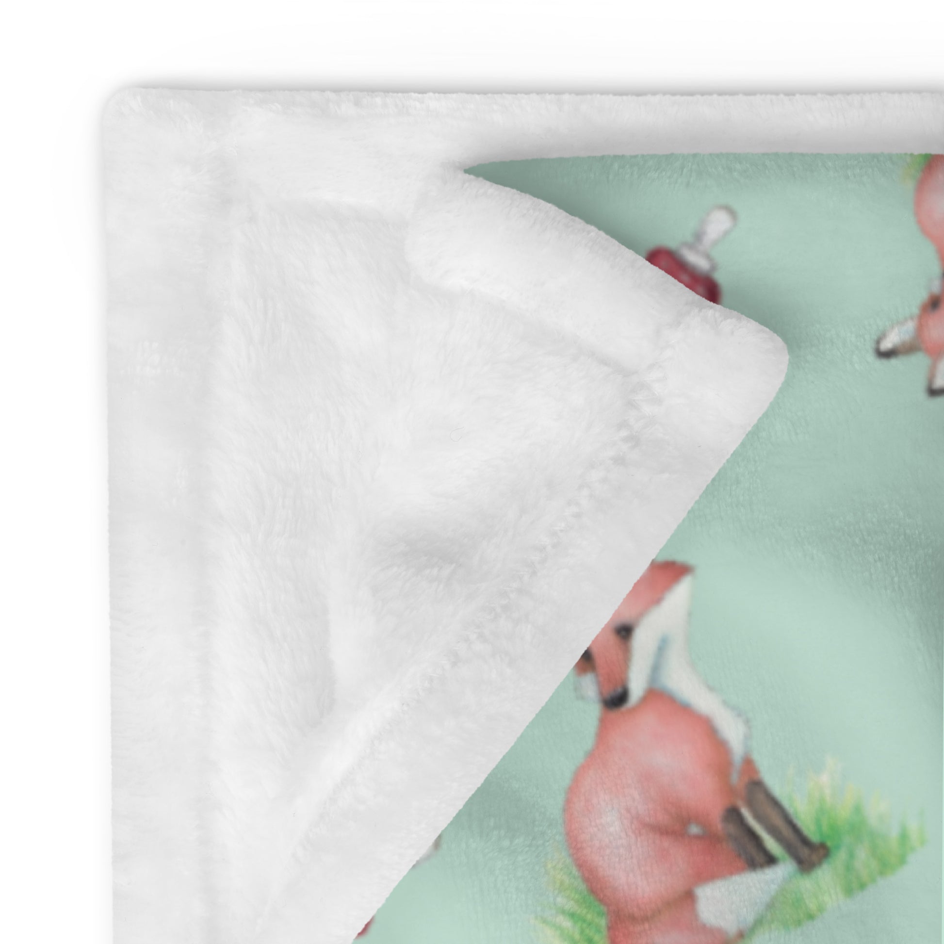 60 by 80 inch watercolor forest fox patterned blanket. Made of soft and fluffy polyester. Has foxes, mushrooms, and ferns on light green background. White underside. Machine-washable, hypoallergenic, and flame retardant. Shown with corner folded over to show white underside.