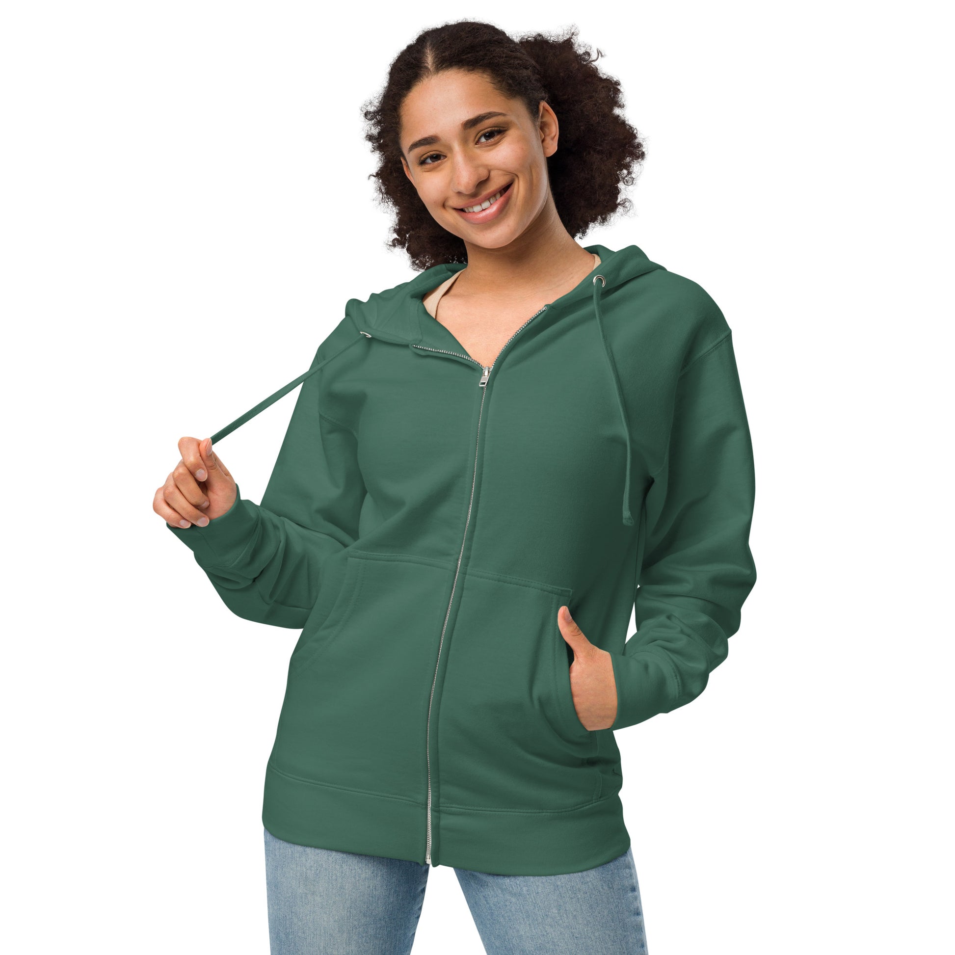 Alpine green colored unisex fleece zip up hoodie. Back design features a watercolor fox in the grass with ferns and mushrooms. Has a jersey-lined hood, metal eyelets and zipper. Front view of hoodie jacket on female model.
