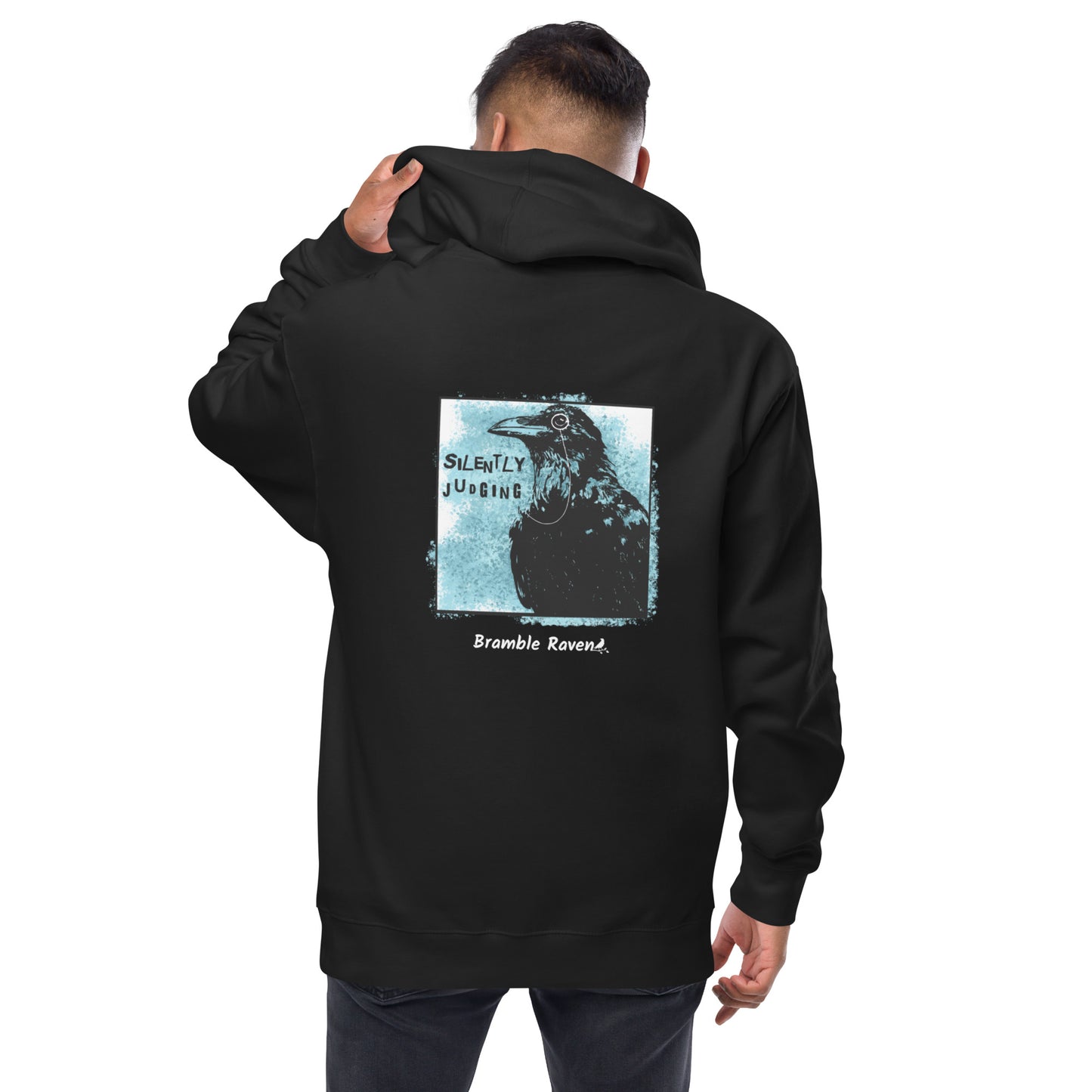 Unisex fleece-lined black colored zip-up hoodie with silently judging text by black crow wearing a monocle in a square with blue paint splatters.  Design on the back of hoodie. Shown on male model.