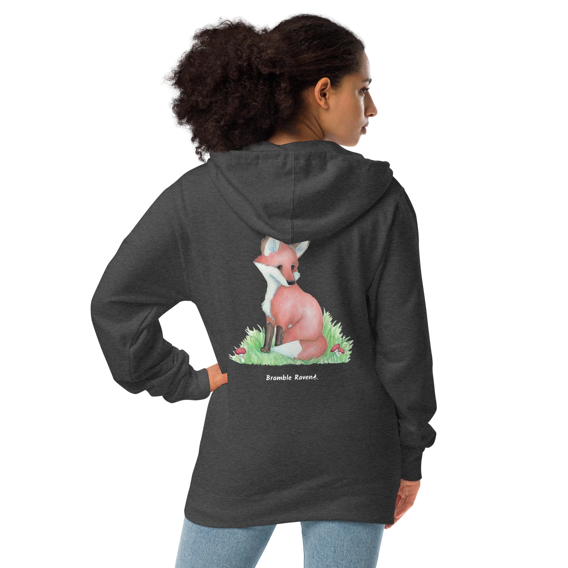 Charcoal heather grey unisex fleece zip up hoodie. Back design features a watercolor fox in the grass with ferns and mushrooms. Has a jersey-lined hood, metal eyelets and zipper. Back view shown on female model.